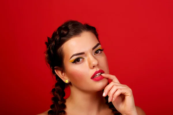 The beauty surprised girl fashion model smiling. Funny braids hairstyle, nails and beige bright makeup, isolated on a red background. Positive emotions smile. Beautiful young woman portrait — Stock Photo, Image