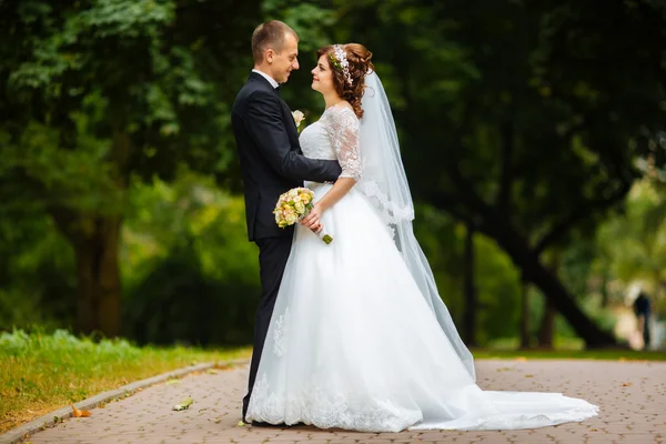 Novia y novio en el día de la boda caminando al aire libre en la naturaleza de otoño. Pareja nupcial, feliz mujer recién casada y hombre abrazándose en el parque verde. Amar pareja de boda al aire libre . — Foto de Stock