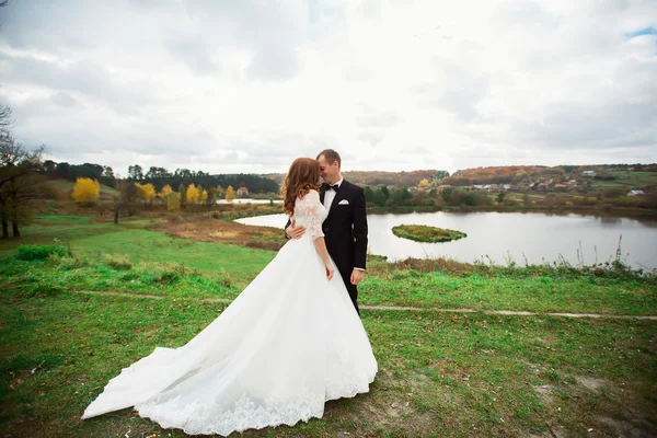 결혼식, 커플 키스 강 근처 언덕에서 일몰에. 긴 베일을 나 부 끼고 바람입니다. 언덕 및 산의 풍경 — 스톡 사진