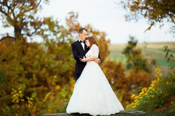 Felice sorridente elegante sposa e sposo passeggiando nel parco verde estivo con mazzo di fiori, ballando e divertendosi il giorno del loro matrimonio — Foto Stock