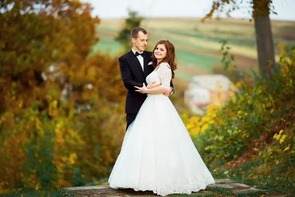 Portrait en gros plan de couples de mariage en amour hipsters mariée dans une robe blanche avec des fleurs et marié dans un costume avec des lunettes et noeud papillon souriant posant étreinte touchante sur un fond de forêt d'automne — Photo