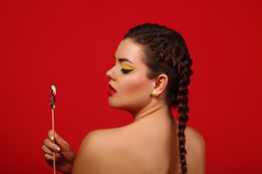 Güzellik moda modeli kız renkli lolipop yemek. Sürpriz komik genç kadınla saç modeli, çivi ve makyaj bej, kırmızı bir arka plan üzerinde izole örgü