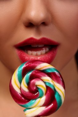 Yakın çekim. Renkli lolipop tutan kırmızı dudaklar esmer kız. Güzellik modeli portre tatlı şekerler kırmızı bir arka plan üzerinde.
