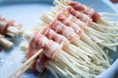 Tayland usulü fırında domuz pastırmalı ızgara iğne mantarı.