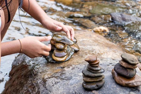 Child hand placing a rock stacks on top of a cairn on creek,Blurred background