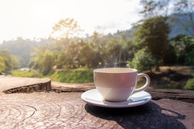 Beyaz bir fincan sıcak espresso kahve fincanı ahşap bir zemine yerleştirilmiş sabah sisi ve güneş ışığı arkaplan dağları, kahve sabahı