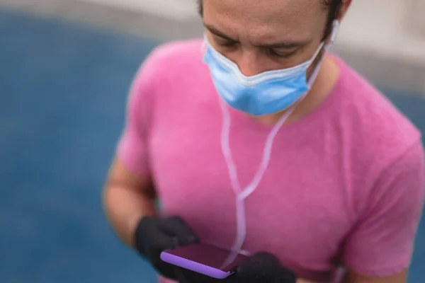 의료용 마스크와 장갑을 스마트폰과 이어폰을 사용하고 환경에서 조깅을 — 스톡 사진