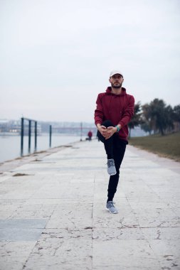 Nehir kenarındaki şehir parkında kapüşonlu sweatshirt 'le antrenman yapan atletik bir sporcu..