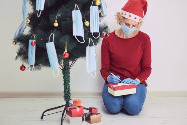 Hediye kutusu olan kadın, 2020 / 2021 virüslü salgın sırasında noel ağacını tıbbi maskelerle süslüyor..