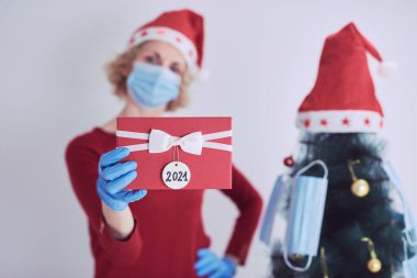 Hediye kutusu olan kadın, 2020 / 2021 virüslü salgın sırasında noel ağacını tıbbi maskelerle süslüyor..