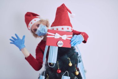 Hediye kutusu olan kadın, 2020 / 2021 virüslü salgın sırasında noel ağacını tıbbi maskelerle süslüyor..