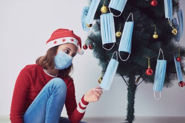 2020 / 2021 yılındaki virüs salgını sırasında küçük bir kız tıbbi maskelerle Noel ağacı süslüyor..
