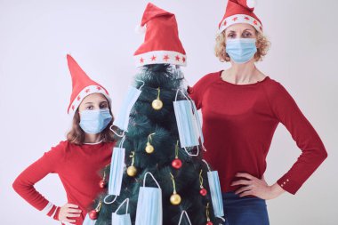 Anne ve kızı 2020 / 2021 virüs salgını sırasında tıbbi maskelerle Noel ağacını süslüyorlar..