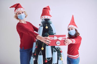 Anne ve kızı 2020 / 2021 virüs salgını sırasında tıbbi maskelerle Noel ağacını süslüyorlar..