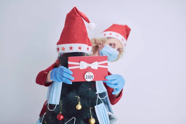 ギフトボックスを持つ女性が存在し ウイルスパンデミック2020 2021中に医療マスクでクリスマスツリーを飾る — ストック写真