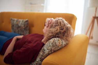 Sinüs ağrısı, baş ağrısı ve mide sorunları olan bir kadın, evdeki bir kanepede yatıyor..