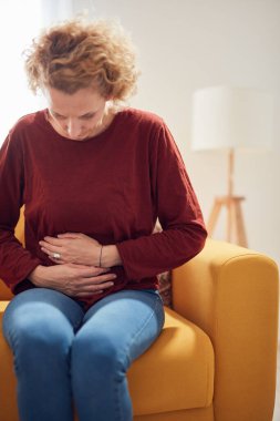Karın ağrısı olan bir kadın evdeki kanepede oturuyor..