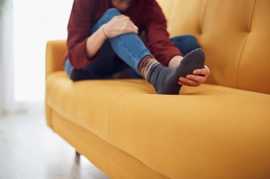 Ayakları çok ağrıyan bir kadın evdeki kanepede oturuyor..