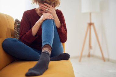 Dizi ve baş ağrısı olan bir kadın evdeki kanepede oturuyor..