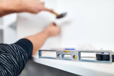 Tamirci tamir ederken çekiç ve ruh seviyesini kullanıyor..