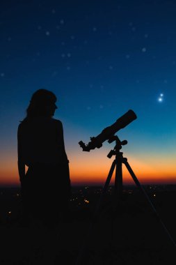 Woman looking at night sky with amateur astronomical telescope. clipart