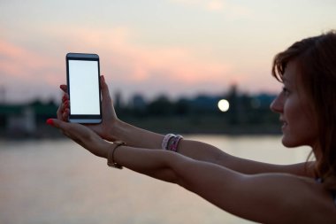 Şehir çevresinde boş beyaz ekranlı cep telefonu tutan genç bir kadın..