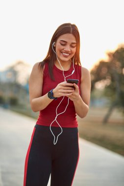 Cep telefonlu modern genç kadın koşu egzersizi sırasında duraksıyor..