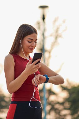Cep telefonlu modern genç kadın koşu egzersizi sırasında duraksıyor..