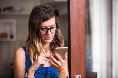 Modern bir evde akıllı telefon kullanan genç bir kadın..