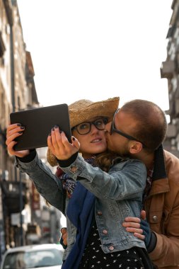 Şehirdeki sokakta selfie çeken genç bir çift..