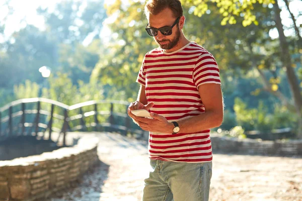 Parkta modern akıllı telefon kullanan genç bir adam..