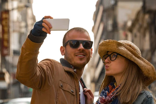 Şehirdeki sokakta selfie çeken genç bir çift..