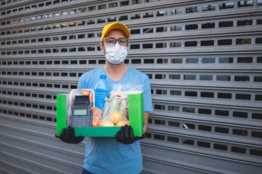 Binanın önündeki koruyucu maskeli teslimatçı bakkaliye ve POS ile temas kurulamayan ödeme kutusuyla..