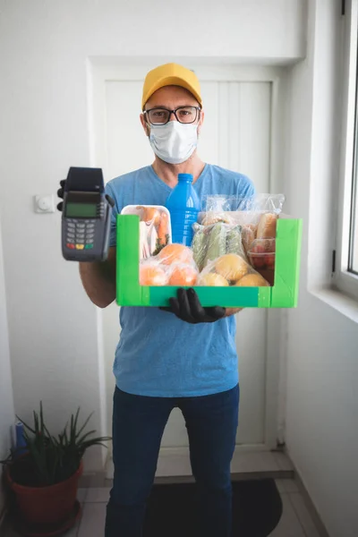 非接触決済のための食料品やPosと保護マスク保持ボックスと自宅のドアの前に配達人 — ストック写真