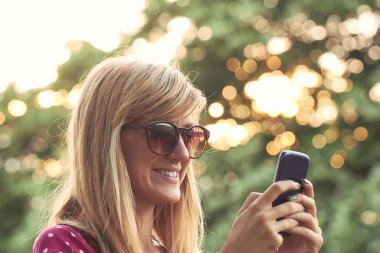 Genç bir kadın açık havada modern akıllı telefon kullanıyor..