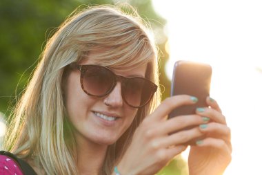 Genç bir kadın açık havada modern akıllı telefon kullanıyor..