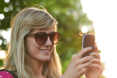 Genç bir kadın açık havada modern akıllı telefon kullanıyor..