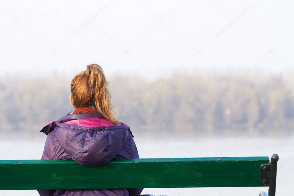 Lonely girl sitting on a bench and looking at the distance.