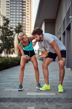 İki sportif genç, kentsel alanda koşup egzersiz yaptıktan sonra duraklıyor..