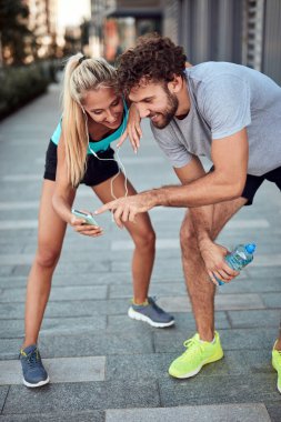 İki sportif genç, kentsel alanda koşup egzersiz yaptıktan sonra duraklıyor..