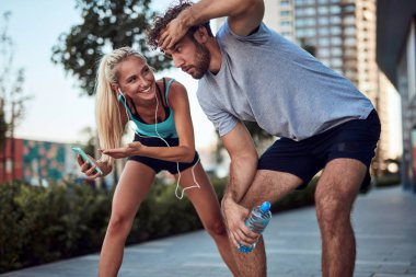 İki sportif genç, kentsel alanda koşup egzersiz yaptıktan sonra duraklıyor..