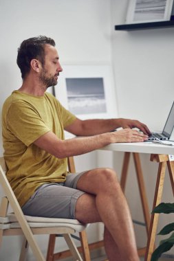 Yetişkin beyaz bir adam evde dizüstü bilgisayarla çalışıyor..