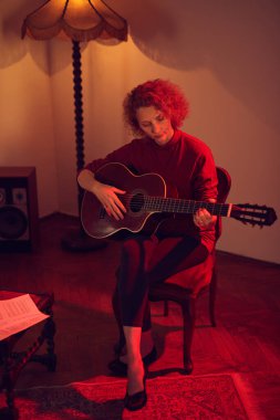Eski moda bir odada akustik gitar çalan bir kadın..