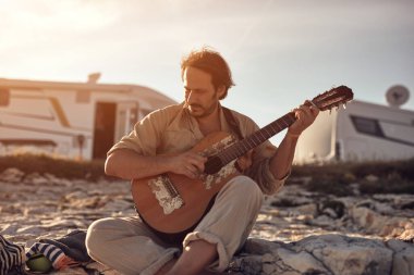 Kamp yapan hippi gitarist yazın deniz kıyısında gitar çalmaktan zevk alıyor..