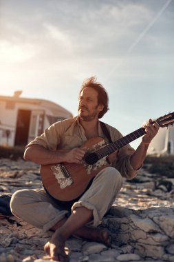 Kamp yapan hippi gitarist yazın deniz kıyısında gitar çalmaktan zevk alıyor..