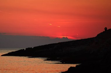 Uzak ufukta gün batımını izleyen bir kadının silueti..