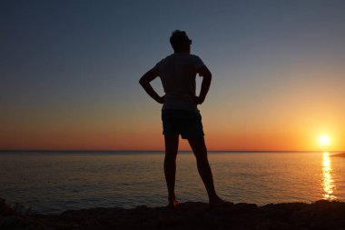 Uzak ufukta gün batımını izleyen bir kadının silueti..