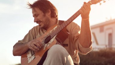 Kamp yapan hippi gitarist yazın deniz kıyısında gitar çalmaktan zevk alıyor..