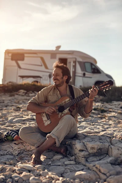 Kamp yapan hippi gitarist yazın deniz kıyısında gitar çalmaktan zevk alıyor..