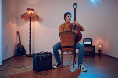 Erkek müzisyen retro vintage odasındaki amplifikatörde akustik gitar çalıyor..